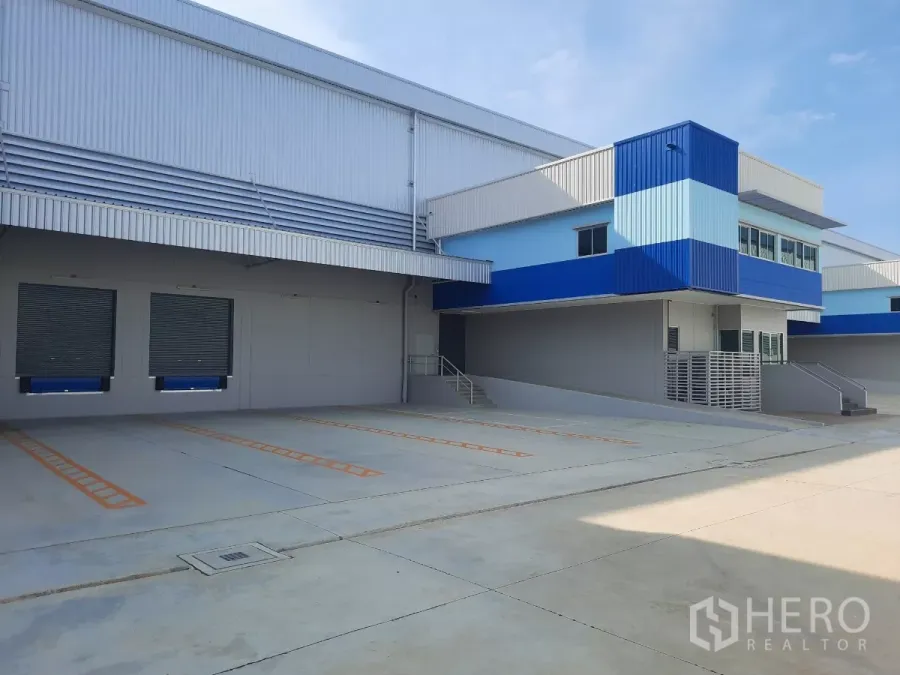 工厂 出租在Bang Lamung, Chon Buri - 现代化仓库外立面，带两个集装箱装卸码头和蓝色办公楼。