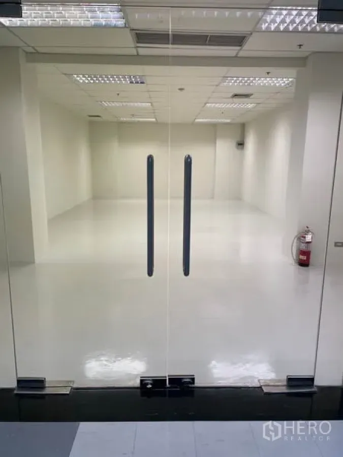 Office Space for rent in Khlong Toei, Bangkok - Glass double doors opening to a bright 55 sqm open-plan office with white floors and grid ceiling lights.