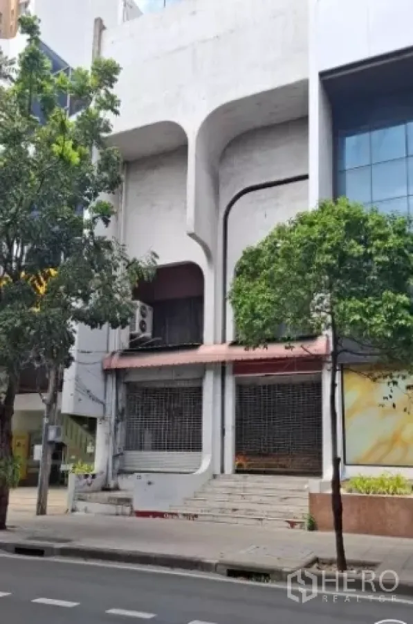 Shophouse for rent in Watthana, Bangkok - Street view of a multi-storey concrete shophouse facade with shuttered storefront and steps.