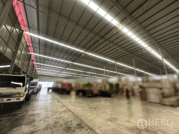 Warehouse for rent in Bang Yai, Nonthaburi - Indoor loading zone with trucks parked along the bay under bright roof panels.