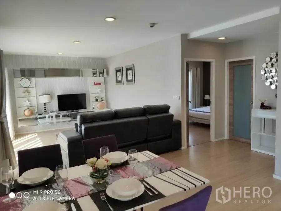 Condominium for rent or sale in Pathum Wan, Bangkok - Spacious open-plan living–dining area with TV feature wall and doorway to bedroom, filled with natural light.