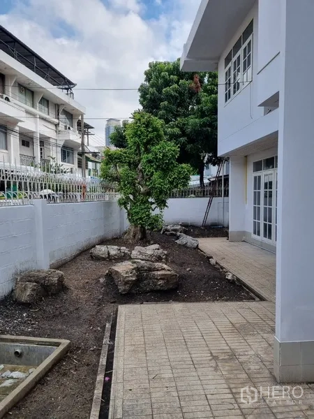 Detached House for rent or sale in Sathon, Bangkok - Side yard with tiled walkway, mature tree and white perimeter wall.