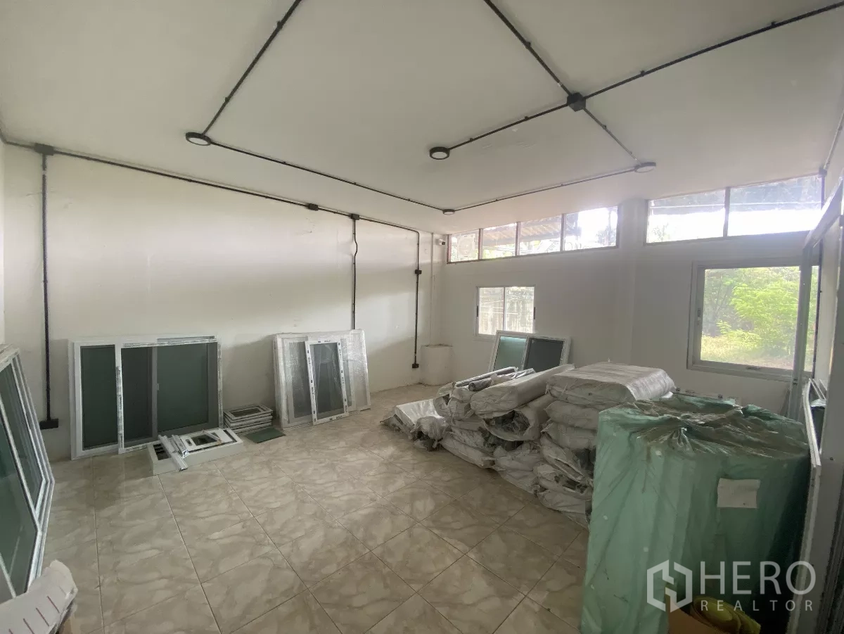 Factory for rent in Mueang Nakhon Pathom, Nakhon Pathom - Utility room with windows, tiled floor, and packaged materials stored inside.
