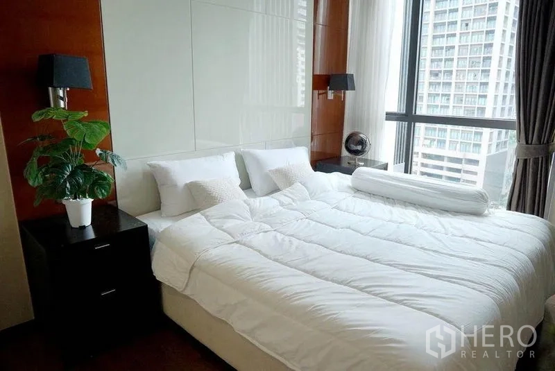 Condominium for rent in Khlong Toei, Bangkok - Sunlit bedroom with large bed, bedside tables, and panoramic windows.