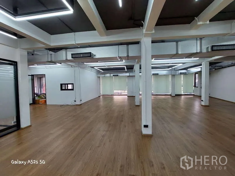 Office Space for rent in Khlong Toei, Bangkok - Spacious open workspace with columns, wood floors and window blinds along one side.