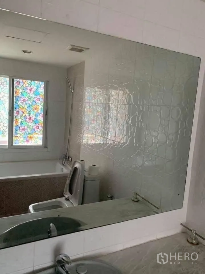 Townhouse for rent in Watthana, Bangkok - Bathroom with bathtub, toilet, large mirror and a window with colorful patterned film.