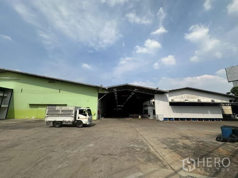 Warehouse for rent in Pak Kret, Nonthaburi - Front view of twin warehouse blocks with wide driveway and loading canopy under clear sky.