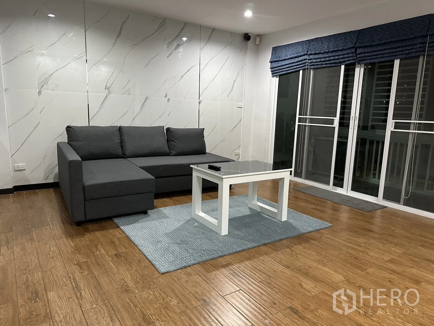 Home Office for rent in Khlong Toei, Bangkok - Living room with marble-look feature wall and sliding glass doors with curtains.