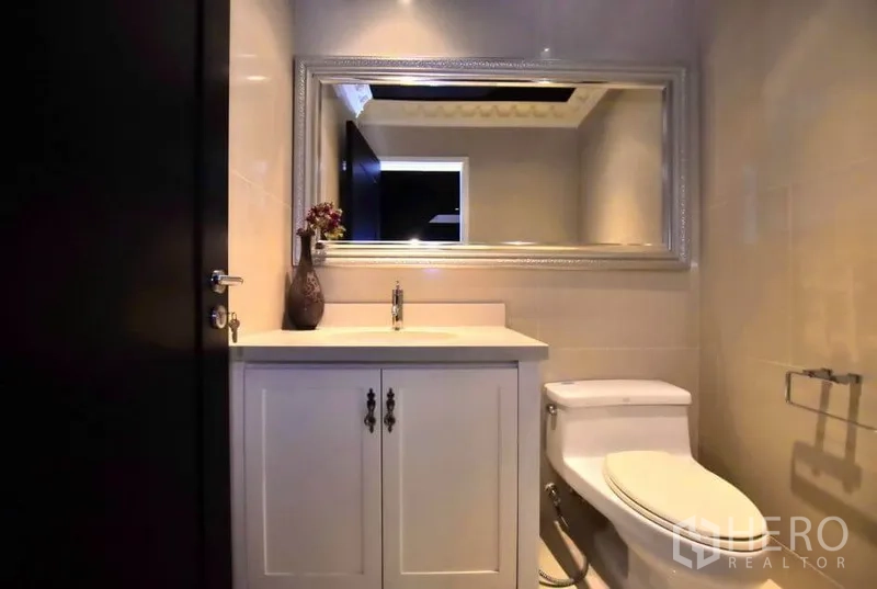 Condominium for rent or sale in Khlong Toei, Bangkok - Guest bathroom with white vanity, large framed mirror and modern toilet.