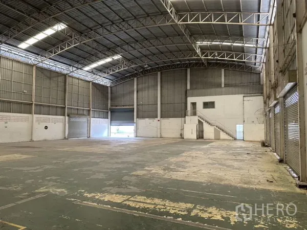 Factory for rent in Phra Nakhon Si Ayutthaya - Spacious warehouse interior with high arched roof, steel trusses, loading doors and a small mezzanine office.