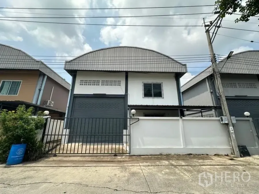 Factory for rent in Bang Bua Thong, Nonthaburi - Front exterior of a mini factory in Pak Kret with roller shutter door, gated entrance and curved metal roof.