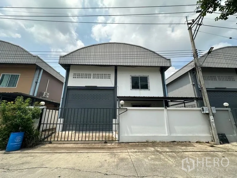 Factory for rent in Bang Bua Thong, Nonthaburi - Front exterior of a mini factory in Pak Kret with roller shutter door, gated entrance and curved metal roof.