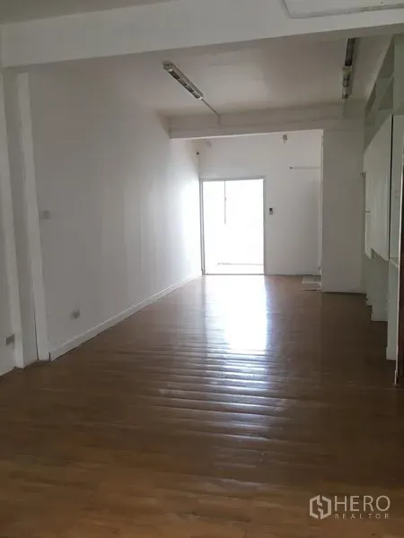 Shophouse for rent in Khlong Toei, Bangkok - Long rectangular room with polished wooden flooring, white walls, and ceiling strip lighting.