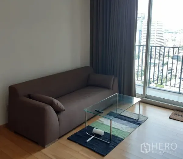 Condominium for sale in Khlong Toei, Bangkok - Bright living room with brown sofa, glass coffee table and balcony city view.