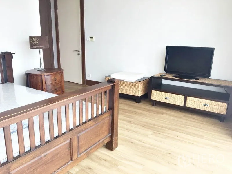 Condominium for rent in Khlong Toei, Bangkok - Bedroom corner with wooden bed, TV stand and basket drawers on wood floors.