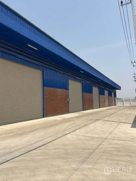 Warehouse for rent in Bang Bua Thong, Nonthaburi - Exterior bays with rolling doors beside a long loading apron and overhead power lines.