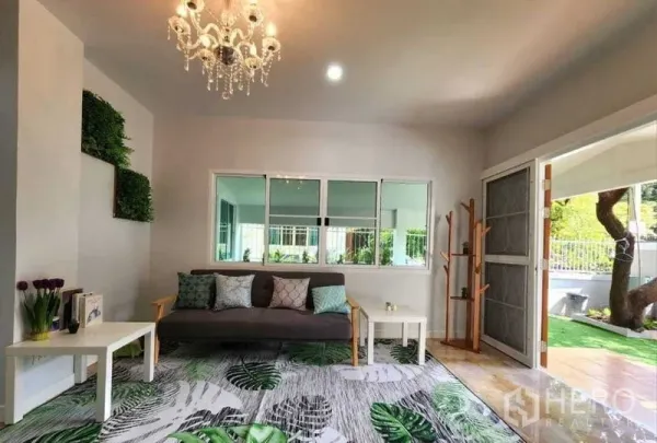 Detached House for rent in Lam Luk Ka, Pathum Thani - Bright living room with chandelier, sofa and large windows opening to the garden.