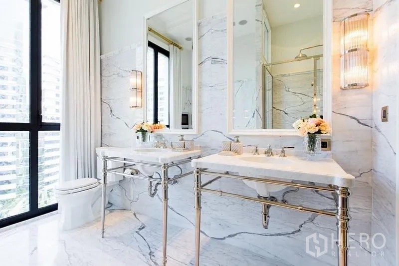 Condominium for sale in Pathum Wan, Bangkok - Marble bathroom with double vanities, large mirrors and glass shower enclosure.