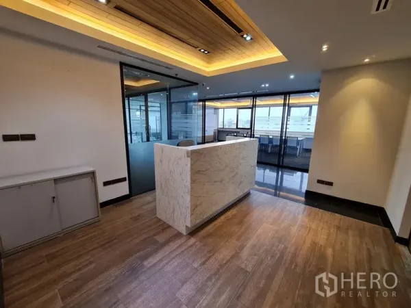Office Space for rent in Bang Rak, Bangkok - Modern reception with marble counter, wood flooring, and glass-partitioned offices under warm recessed lighting.