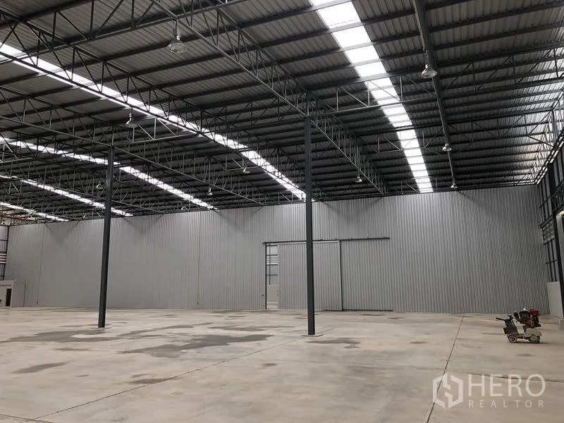 Warehouse for rent in Lat Krabang, Bangkok - Wide-span warehouse showing corrugated metal walls, skylights, and a large sliding door opening.
