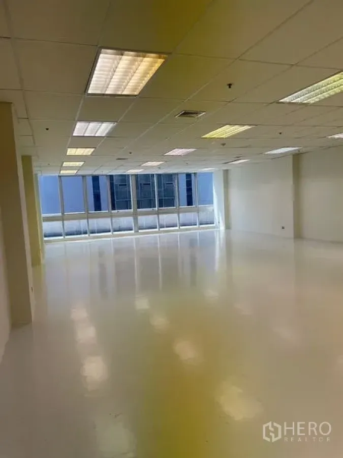 Office Space for rent in Watthana, Bangkok - Spacious office with grid ceiling lights, white flooring, and city-facing windows.