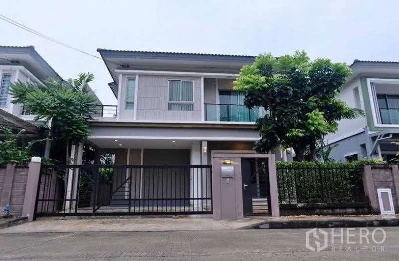 Detached House for rent in Suan Luang, Bangkok - Front elevation of gated two-storey house with balcony and landscaped hedge.
