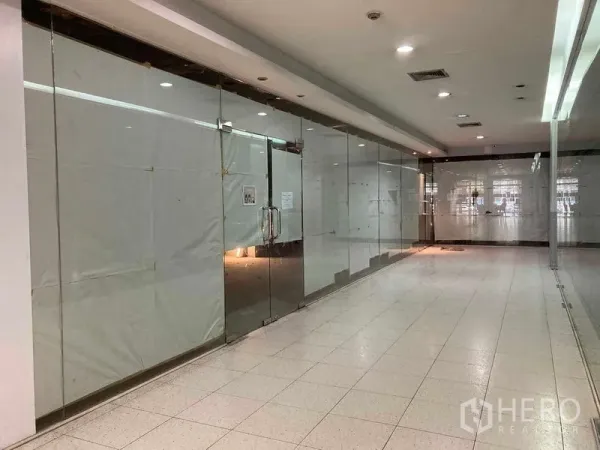 Retail Space for rent - Empty retail shopfront with full-height glass doors along an indoor shopping corridor, tiled flooring and ceiling lights.