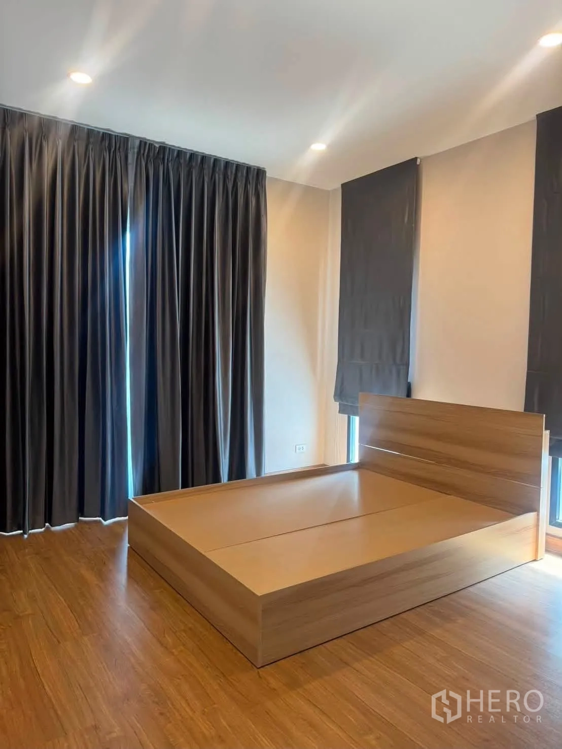 Detached House for rent or sale in Prawet, Bangkok - Spacious bedroom with wooden bed, dark blackout curtains, recessed lights, and wood floors.