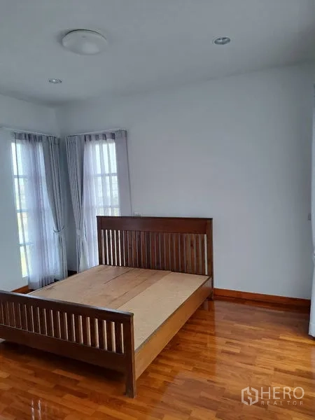 Detached House for rent in Prawet, Bangkok - Secondary bedroom with wooden bed frame, two narrow windows and sheer curtains.