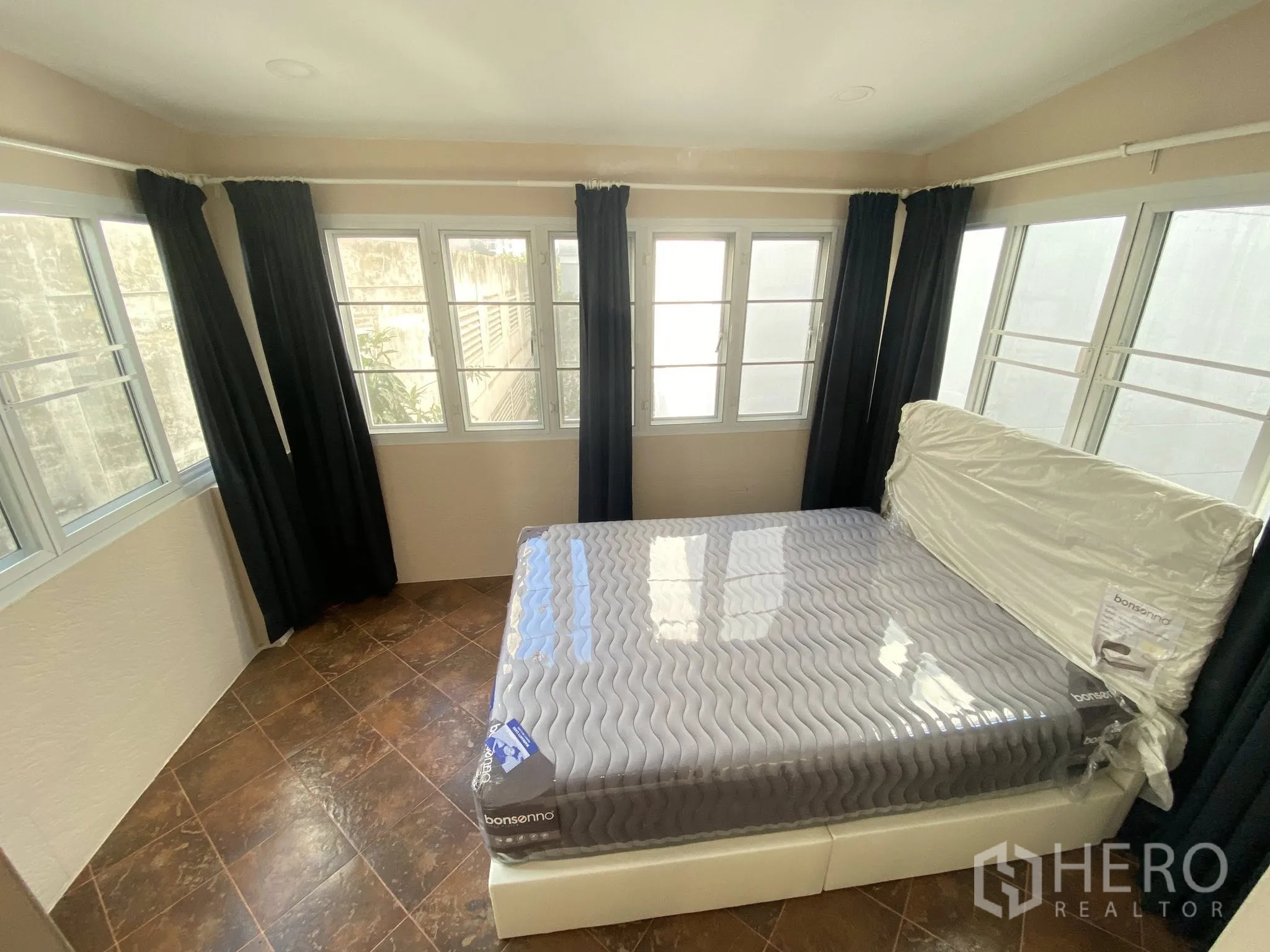 Home Office for rent in Pathum Wan, Bangkok - Corner bedroom surrounded by multiple windows with blackout curtains and tiled flooring.