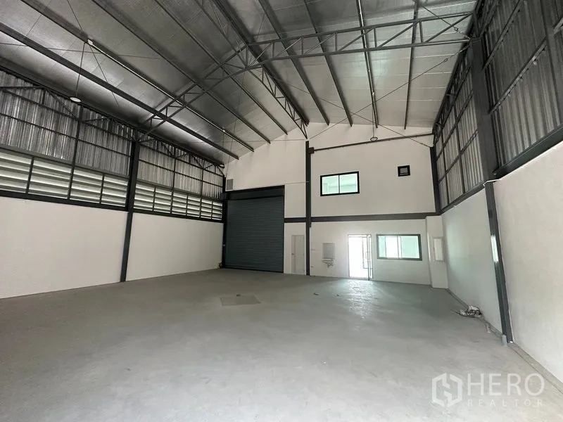 Factory for rent or sale in Bang Bua Thong, Nonthaburi - Warehouse interior facing the roller shutter with office windows and a wall sink.