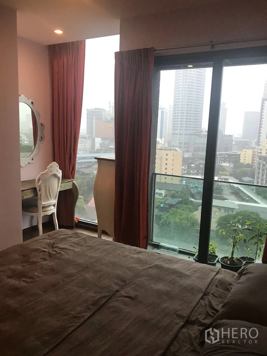 Condominium for rent in Khlong Toei, Bangkok - Bedroom with vanity corner and balcony overlooking the Bangkok skyline.