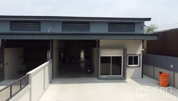 Warehouse for rent in Bang Bua Thong, Nonthaburi - Front facade of the warehouse with wide roller shutter, office window, ventilation louvres and spacious forecourt.