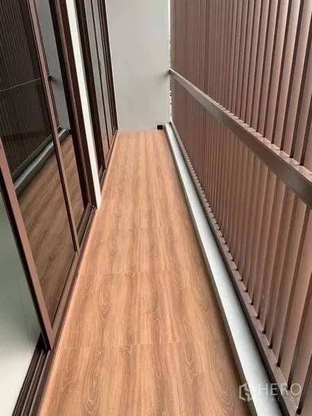 Shophouse for rent in Suan Luang, Bangkok - Narrow balcony with wood-look tiles and brown vertical screen beside sliding glass doors.