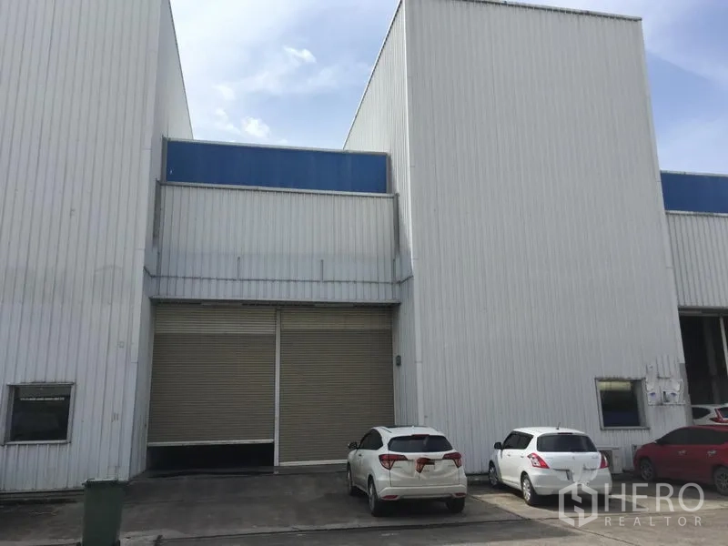 Factory for rent in Khlong Luang, Pathum Thani - Factory facade featuring a large roller shutter door with on-site car parking at a contemporary warehouse unit.