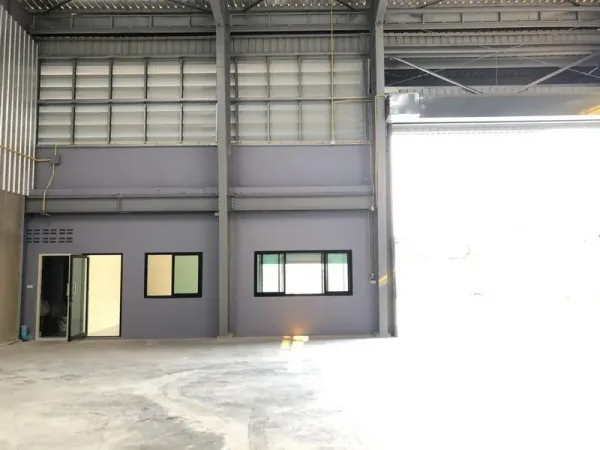 Factory for rent in Khlong Luang, Pathum Thani - Interior showing a ground-floor office block beneath a tall steel roof and wide roller door.