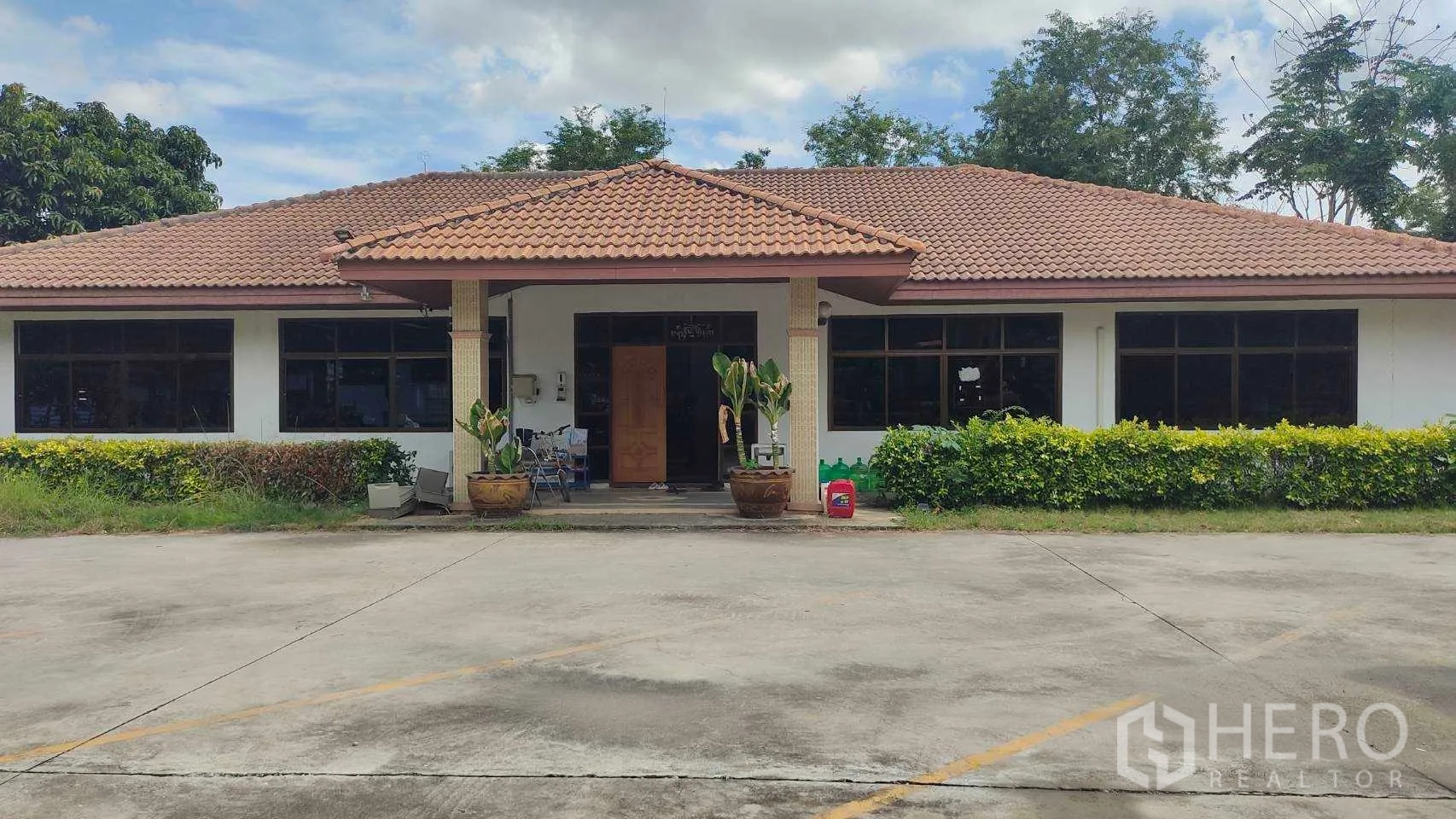 Factory for sale in Nikhom Phatthana, Rayong - Single-storey office building with tiled roof, front porch and landscaped shrubs.