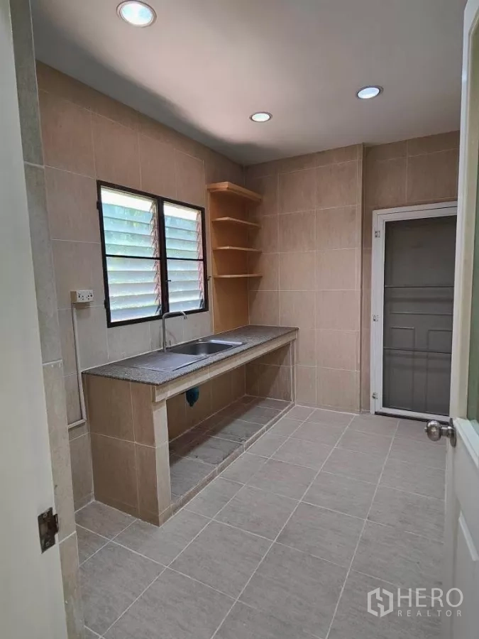 Detached House for rent or sale in Mueang Nonthaburi, Nonthaburi - Separate Thai kitchen with long counter, sink, shelving and rear door.