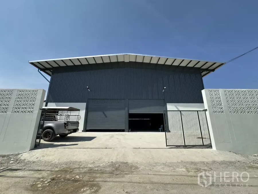 Warehouse for rent in Prawet, Bangkok - Front view of modern steel-clad warehouse with wide roller shutters, gate and parking apron in Prawet, Bangkok.