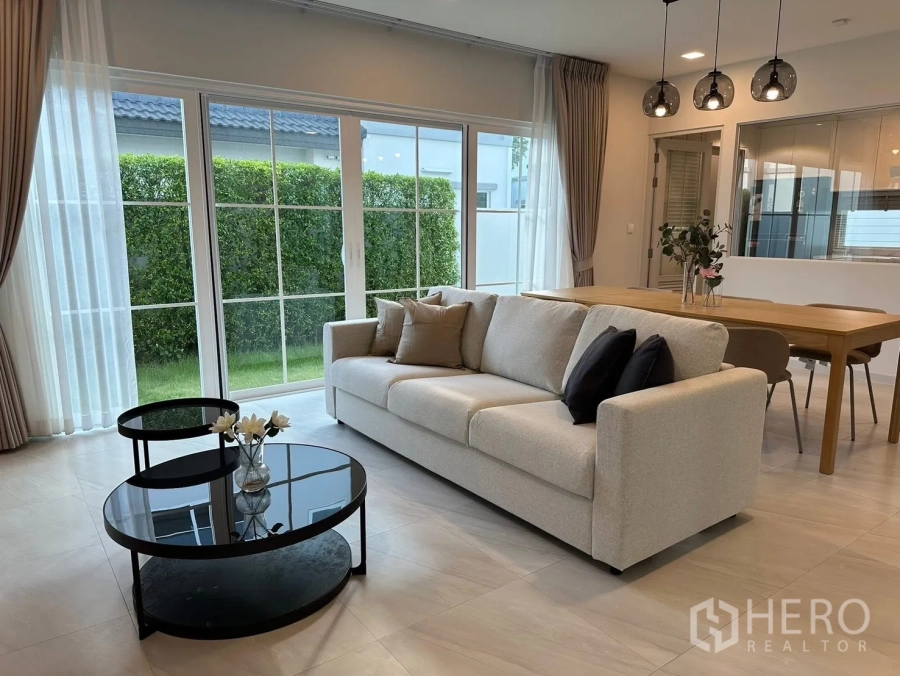 Detached House for rent in Bang Phli, Samut Prakan - Living room with sofa, coffee table, dining set, and wide glass doors.