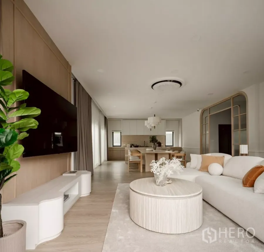 Detached House for rent in Bang Phli, Samut Prakan - Open-plan living room with TV wall, round coffee table, light wood floors and view to the dining kitchen
