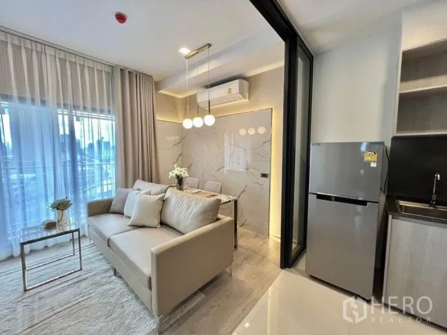 Condominium for rent in Watthana, Bangkok - Living area open to kitchenette with stainless refrigerator and sliding glass divider.