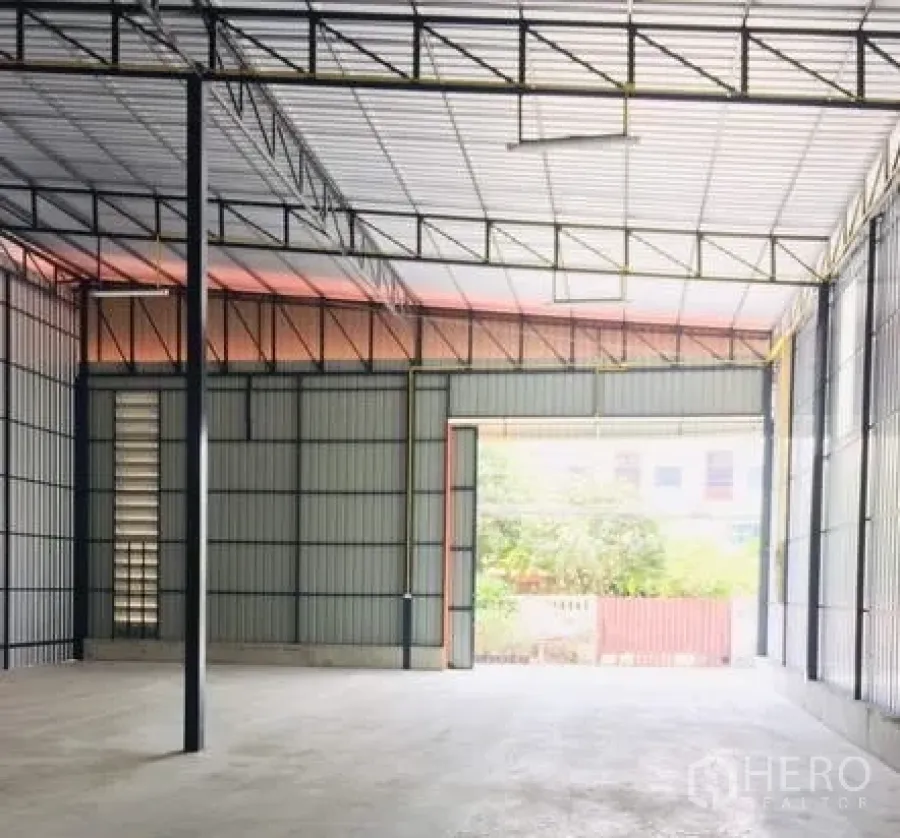 Warehouse for rent in Bang Kapi, Bangkok - Spacious warehouse interior with high steel truss roof, concrete floor, and a wide loading door allowing truck access.