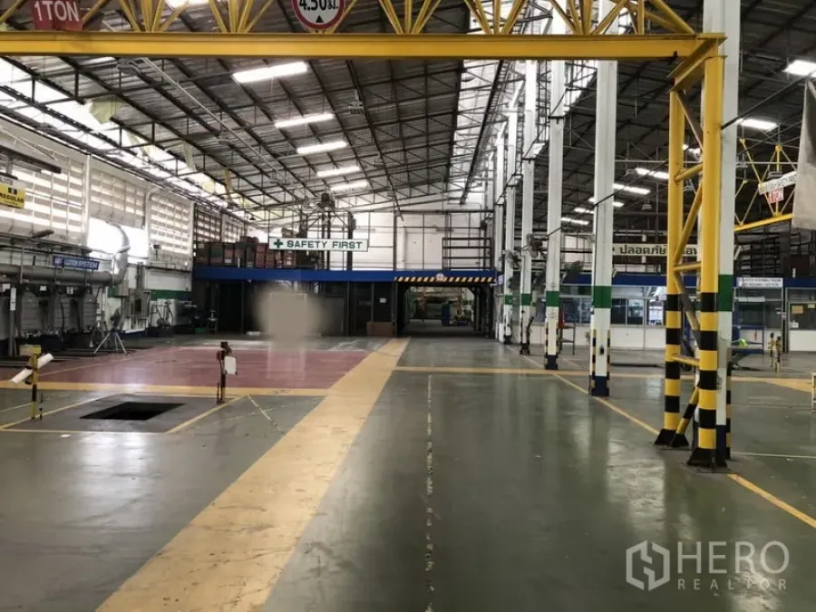 Factory for rent in Lam Luk Ka, Pathum Thani - Wide central aisle beneath a yellow crane with striped safety columns and ventilated walls.