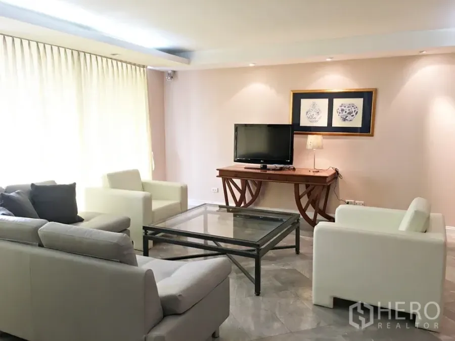 Condominium for rent in Pathum Wan, Bangkok - Sunlit living room with white sofas, glass coffee table, and a TV on a console table.