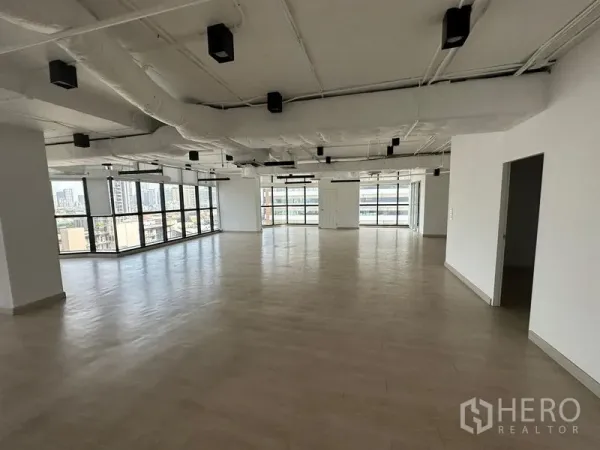 Office Space for rent - Spacious open‑plan office with light wood floors, exposed ceiling and wraparound windows overlooking the Bangkok skyline.