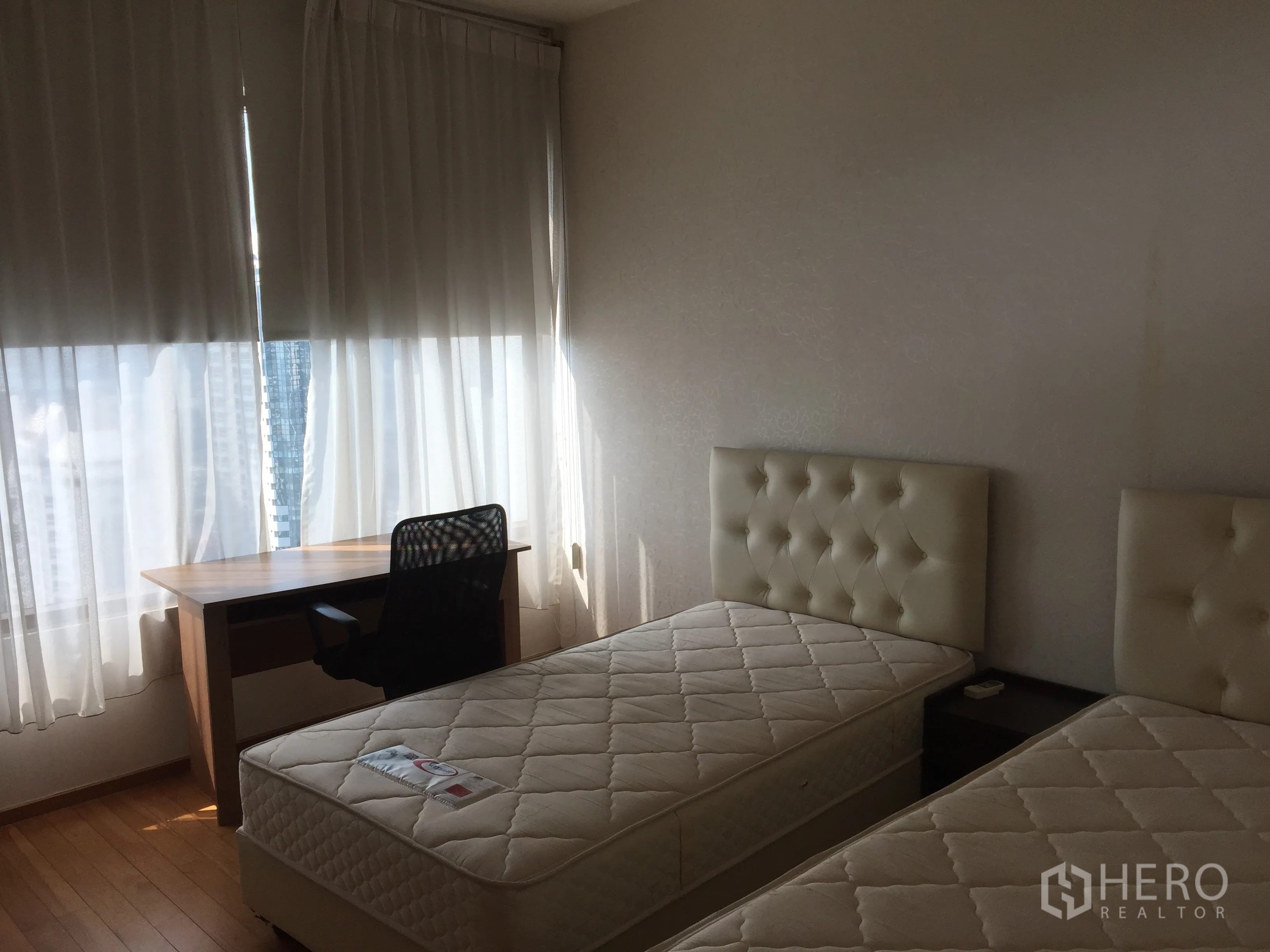 Condominium for rent or sale in Khlong Toei, Bangkok - Second bedroom with twin beds, study desk, wooden floor, and a large window with light curtains.