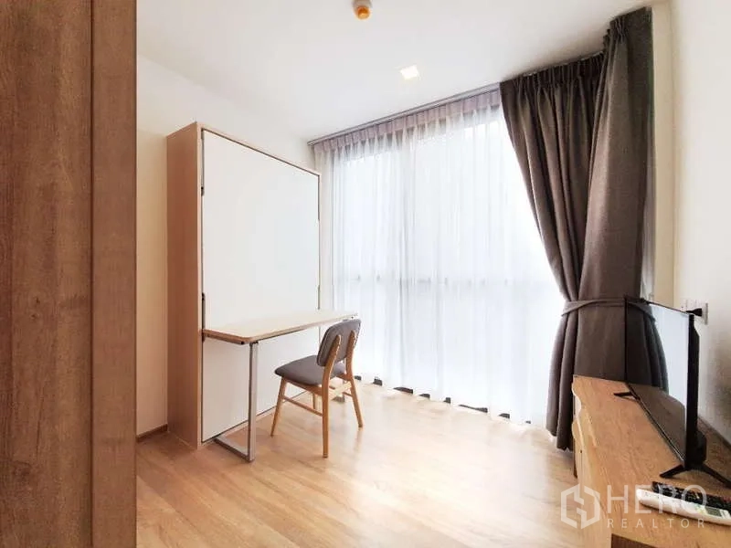 Condominium for sale in Watthana, Bangkok - Flexible second bedroom with Murphy bed folded up and study desk by a full-height window.