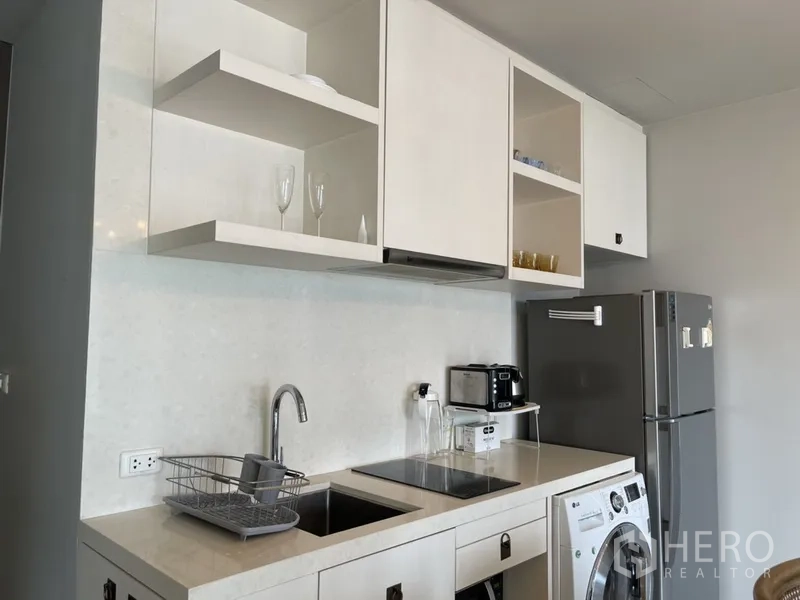 Condominium for rent in Bangkok - Modern kitchenette with induction hob, sink, open shelves, and refrigerator.