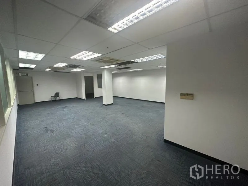 Office Space for rent in Khlong Toei, Bangkok - Open‑plan workspace with blue carpet, grid ceiling lights, columns and interior windows.